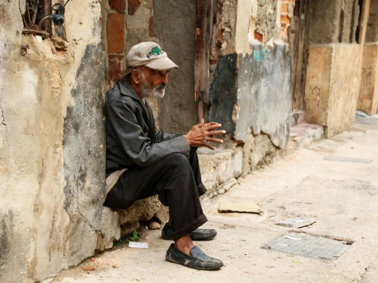 an old man sitting on the street holding soing up to his mouth