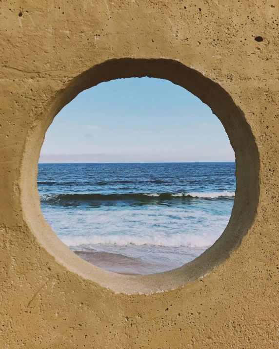 the ocean looks incredible through an arch in a sandy wall