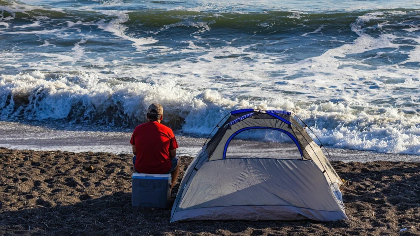 a man is sitting next to a tent near the ocean