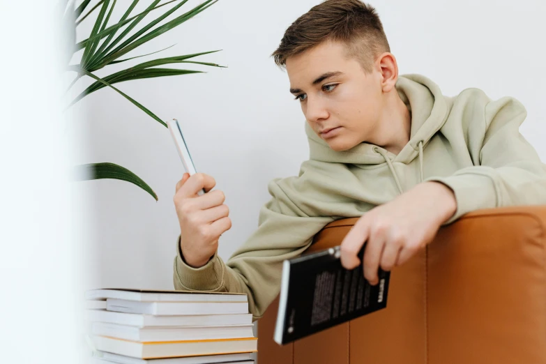 a young man holding a cell phone near a stack of books