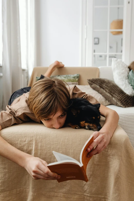 woman lying on couch holding open book next to her face