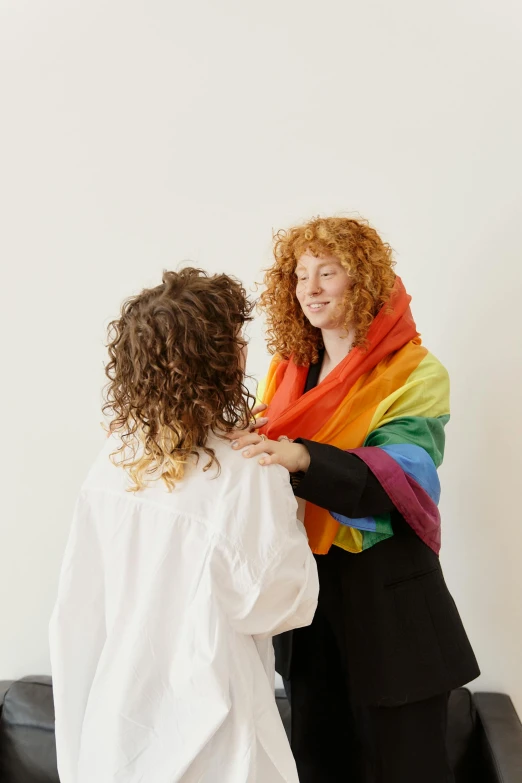 two women are dressed in white dresses and a rainbow colored scarf