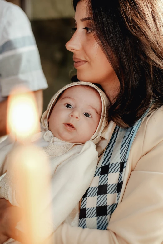 a woman with a baby in a sling holding a candle