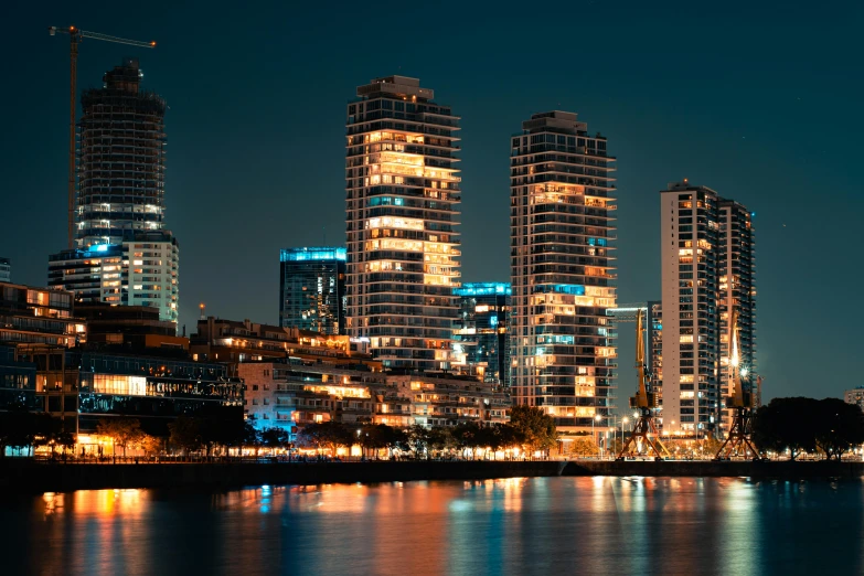 some large buildings along the waterfront with lights on