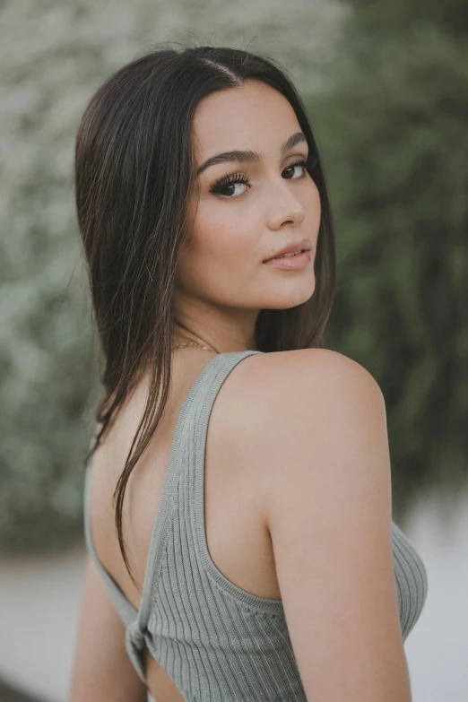 a girl in a gray tank top stands with her head turned