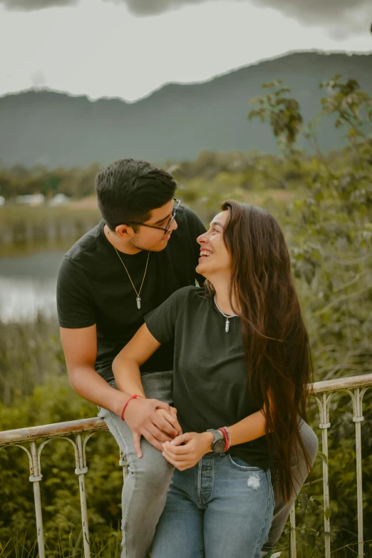 a man holding onto the arm of his girlfriend as they stand together on a balcony with mountains in the background