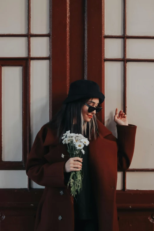 a woman is holding a bunch of flowers and posing in front of a wooden door