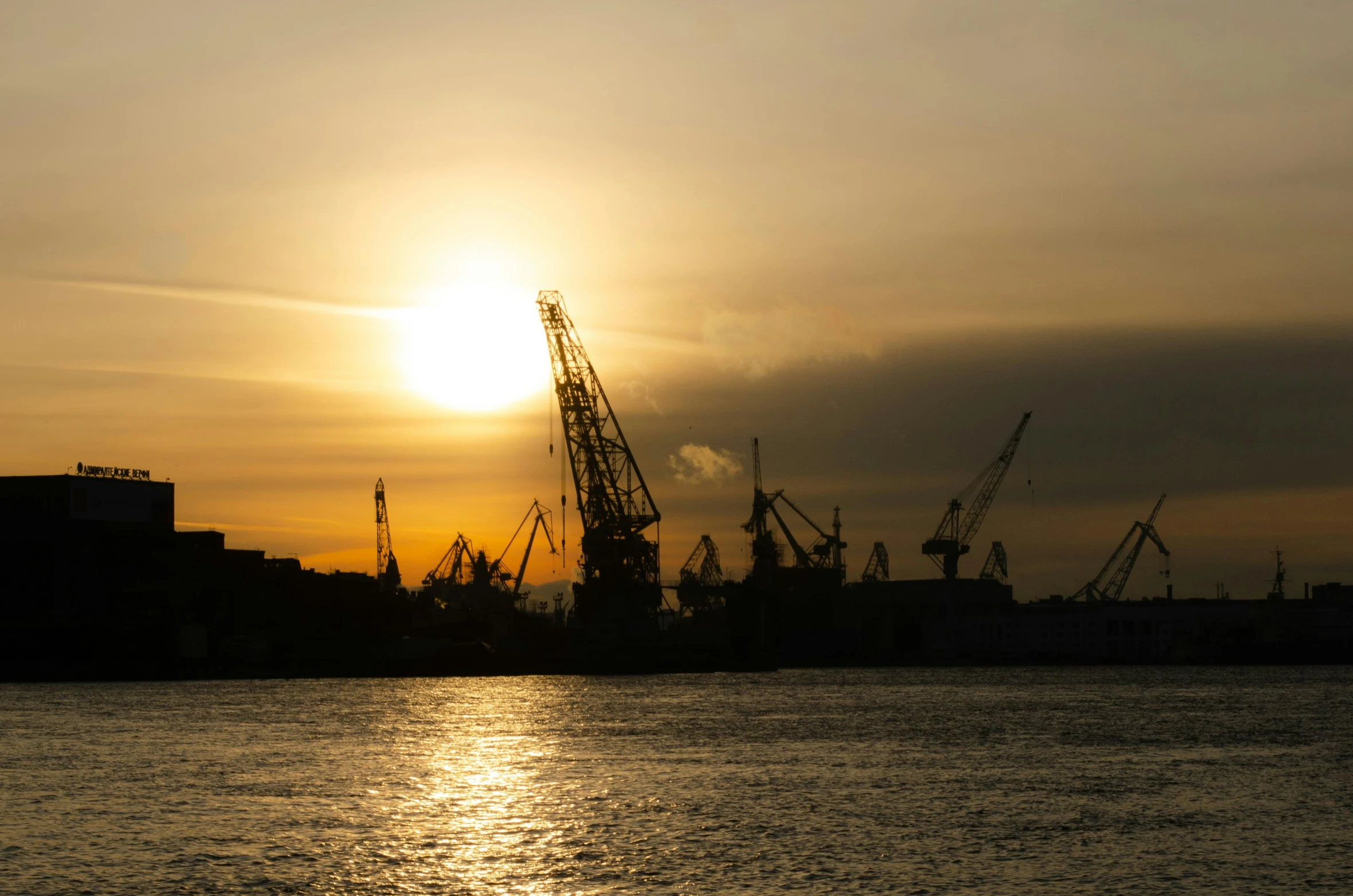 two cranes in the distance are silhouetted against the setting sun