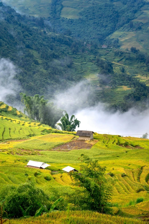 fog is rolling in over the mountains surrounding a farm