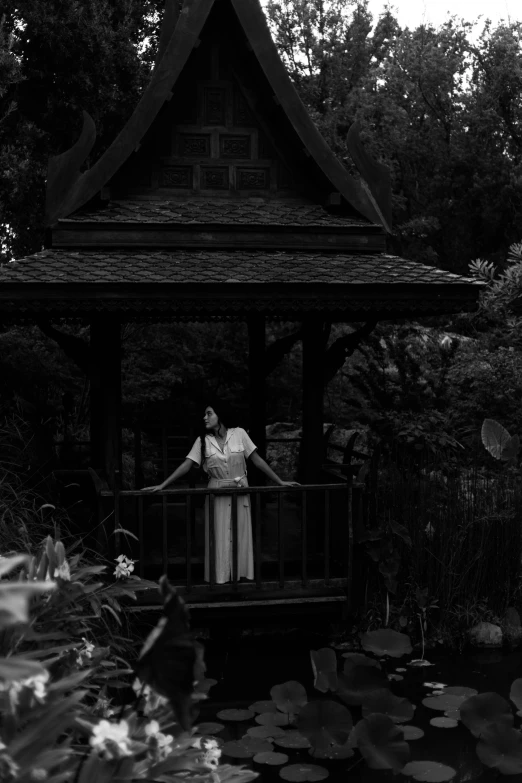 woman standing on platform near lily pond, in black and white