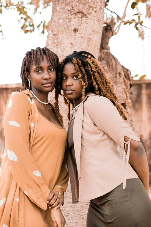 two women standing next to each other with a tree in the background