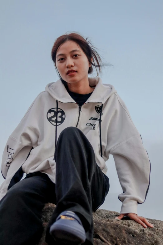 a young woman sitting on top of a rock in a sweatshirt