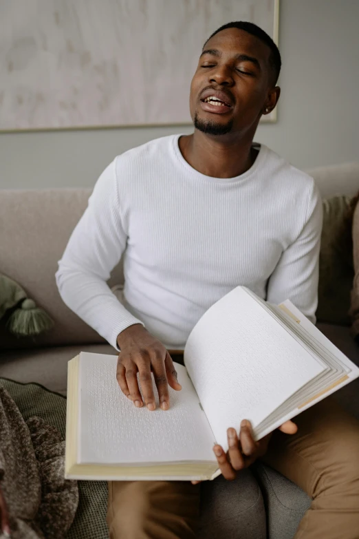 a black man sitting on a couch looking into the air while holding a book in his hands