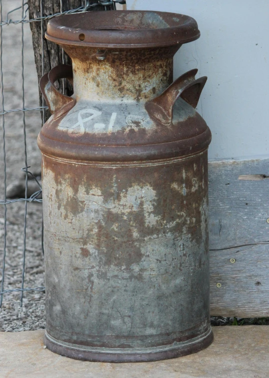 a rusted barrel sitting next to a wire fence