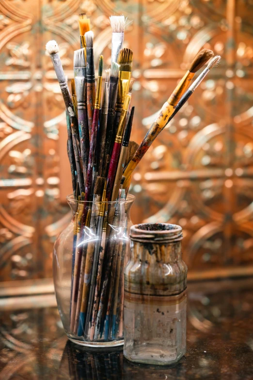 an assortment of art paint and pencils are in a clear glass