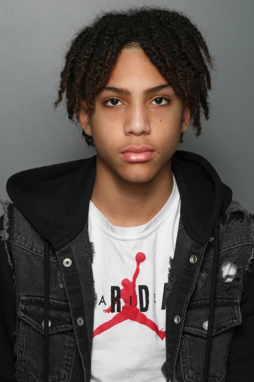 young man with dreadlocks on his hair in front of a gray wall