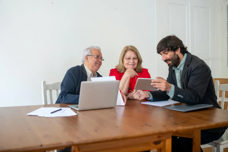 three people are sitting around a table looking at a computer