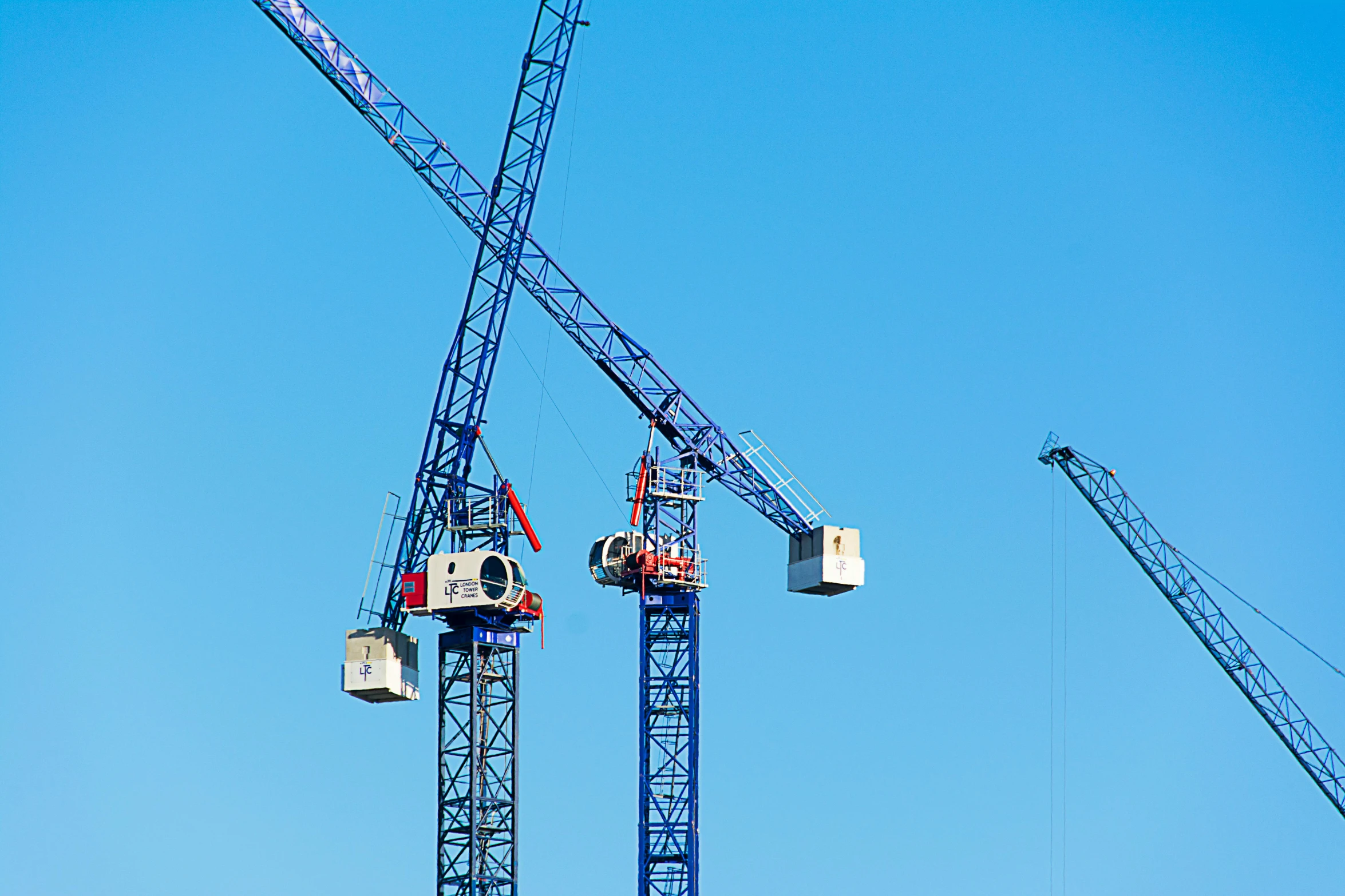 many cranes are near a building under a clear blue sky