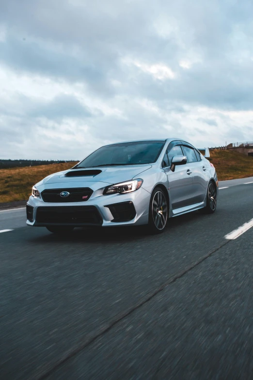 a silver car driving down the road in front of cloudy skies