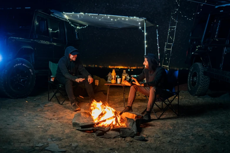 two people sitting around an open fire in a campground