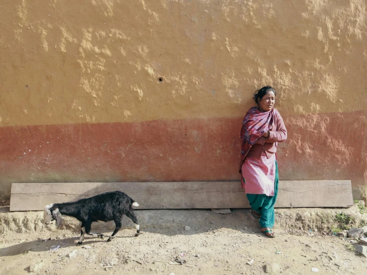 a woman standing against a wall beside a small animal