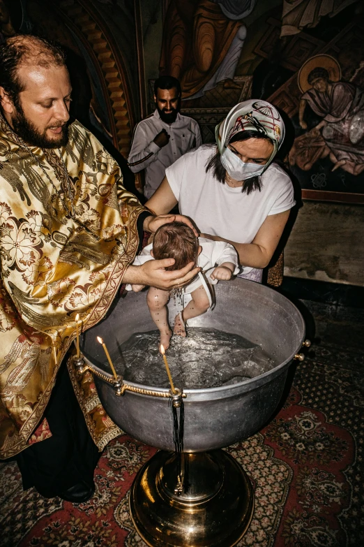 a man in a priest's robes holding a baby in an ice bucket