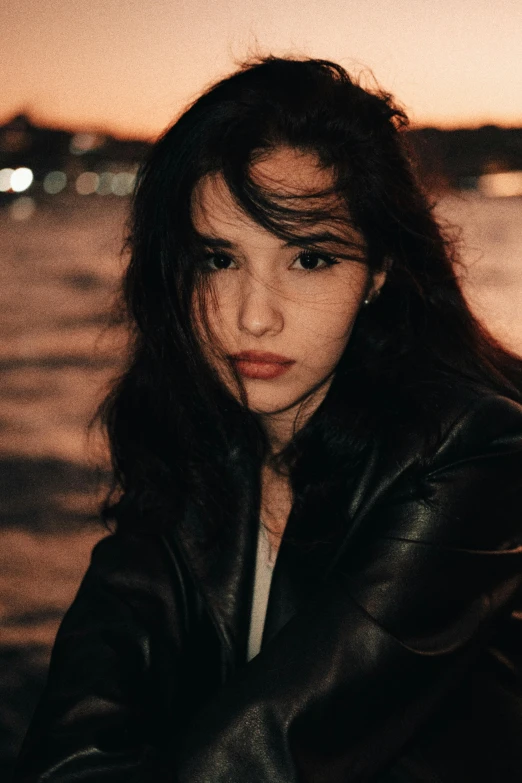 the girl has long dark hair and is sitting at the edge of the water