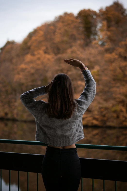 a girl in a crop top and jeans standing on a bridge looking at trees