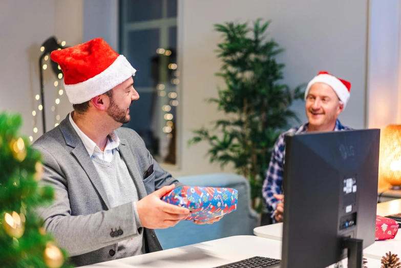 two men are sitting at a computer wearing christmas hats