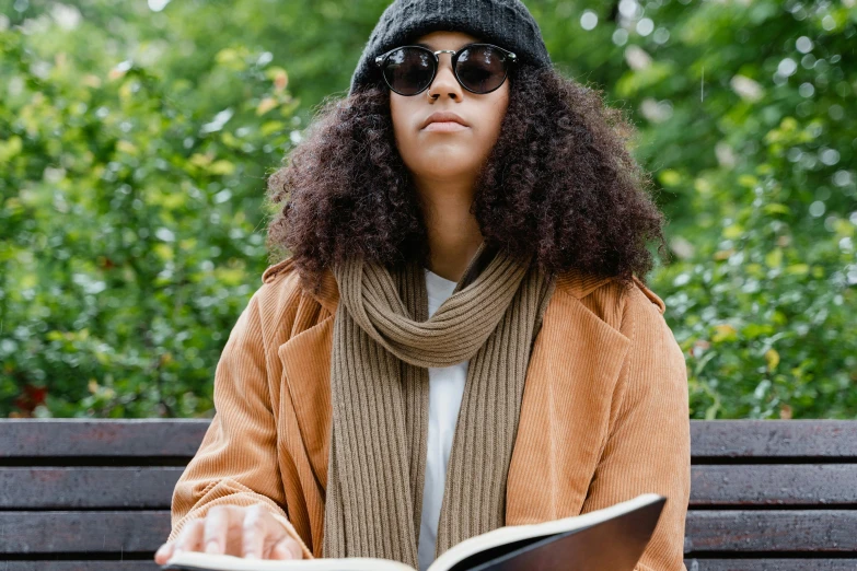 a woman in brown coat sitting on a bench and reading a book