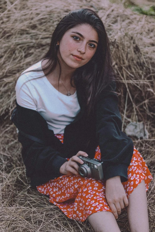 a beautiful young woman holding a camera posing in some dry grass