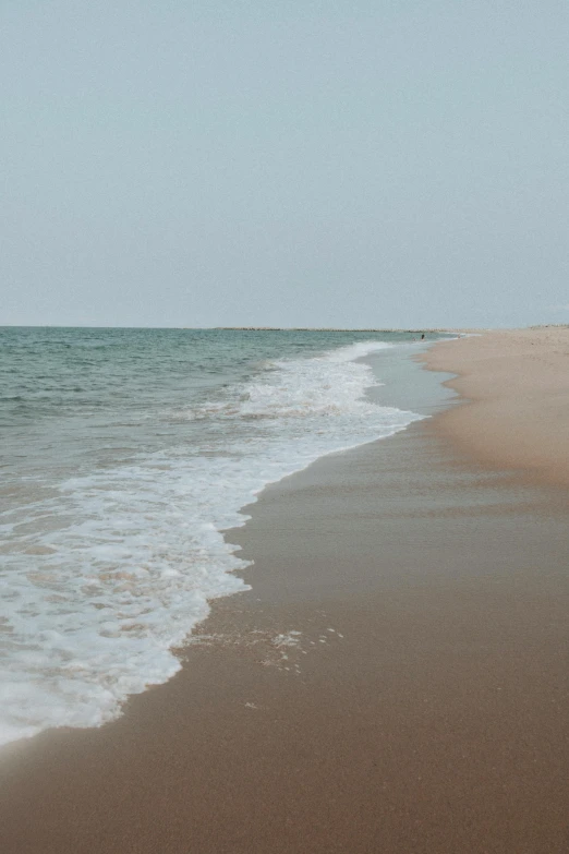 an empty beach with a person carrying a surf board