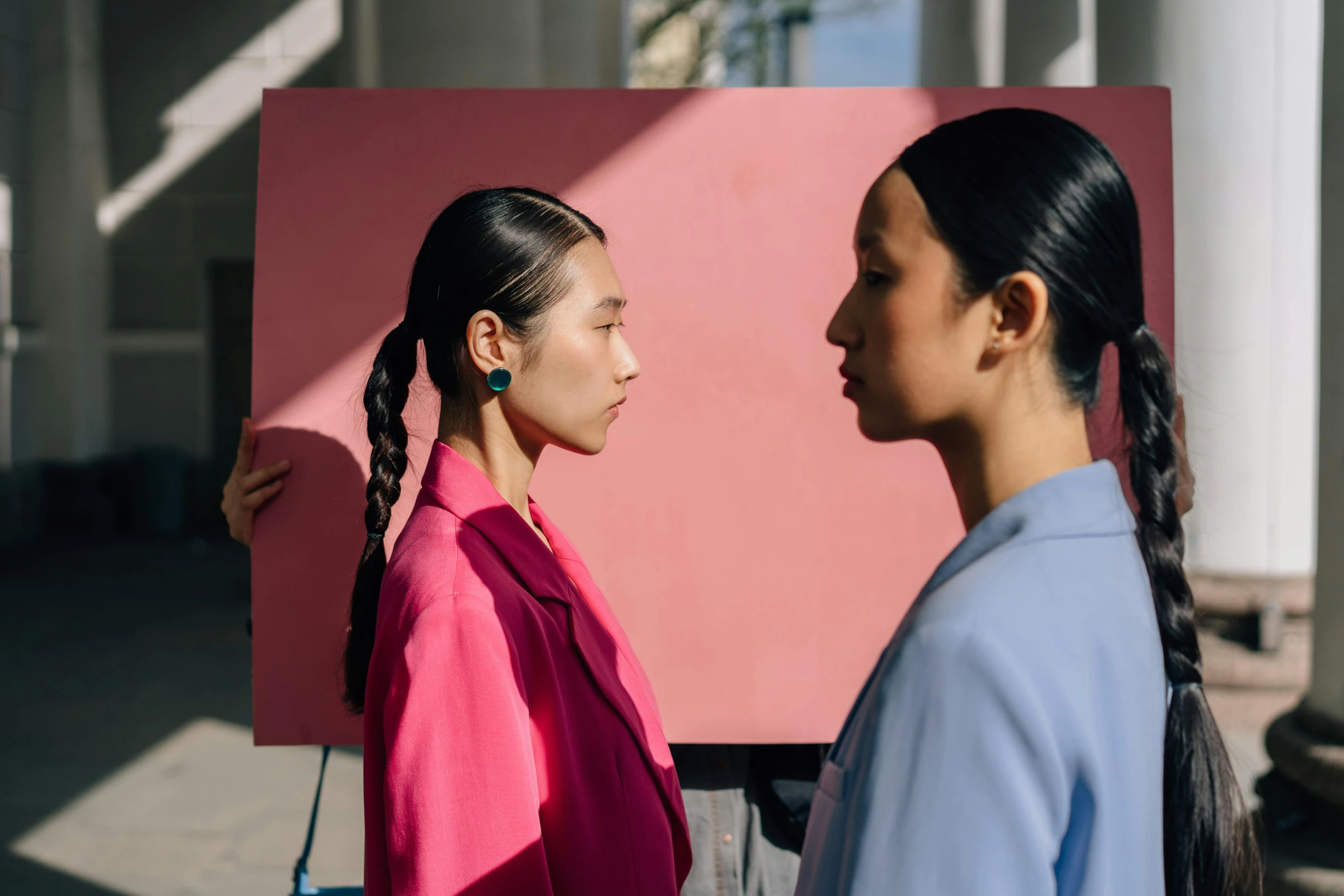 two women standing in front of a pink piece of paper