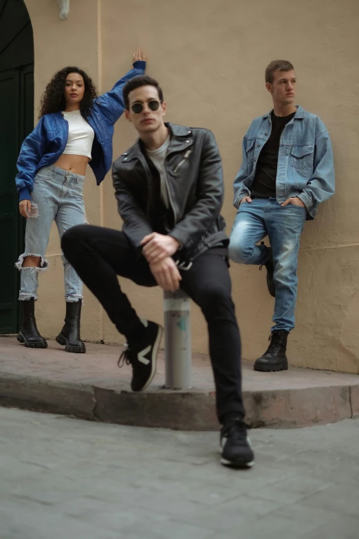 three people sitting and one standing near a building