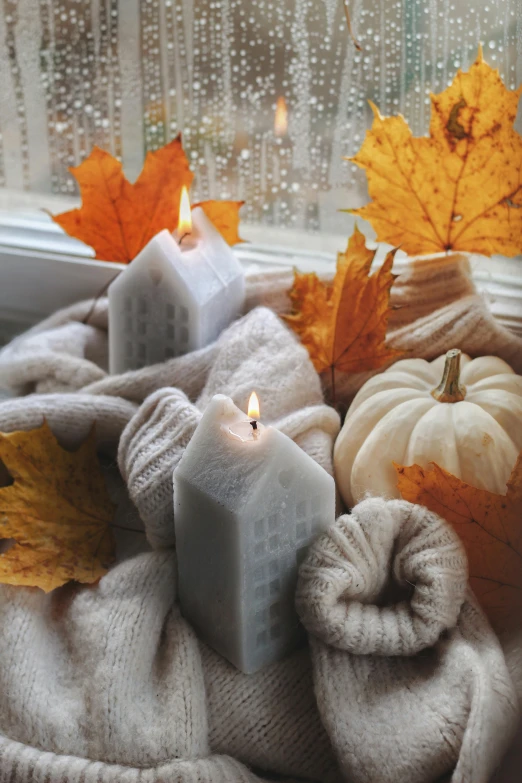 a candle, scarf and autumn leaves are placed together on the windowsill