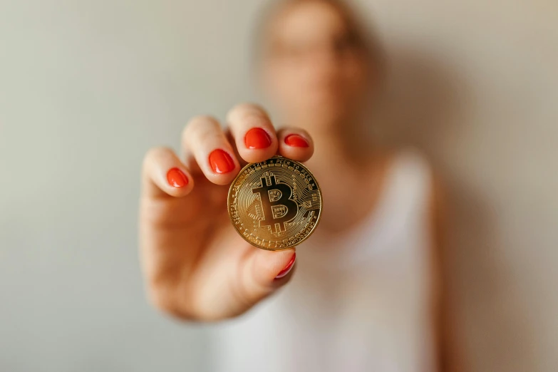 a woman with orange nail polish holds up her gold coin