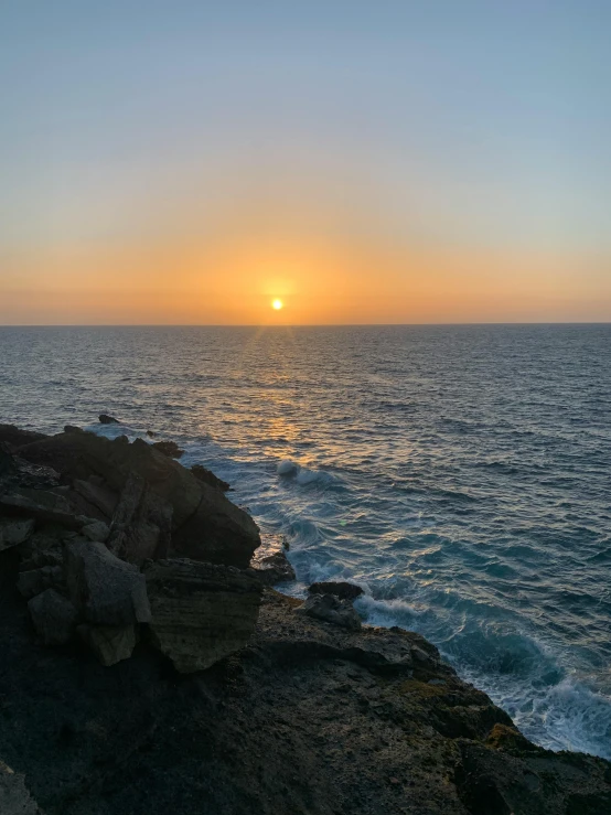 the sun is setting over the ocean with the rocks