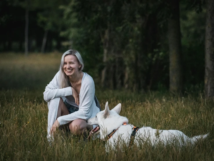 a beautiful blond woman sitting on the grass with a dog