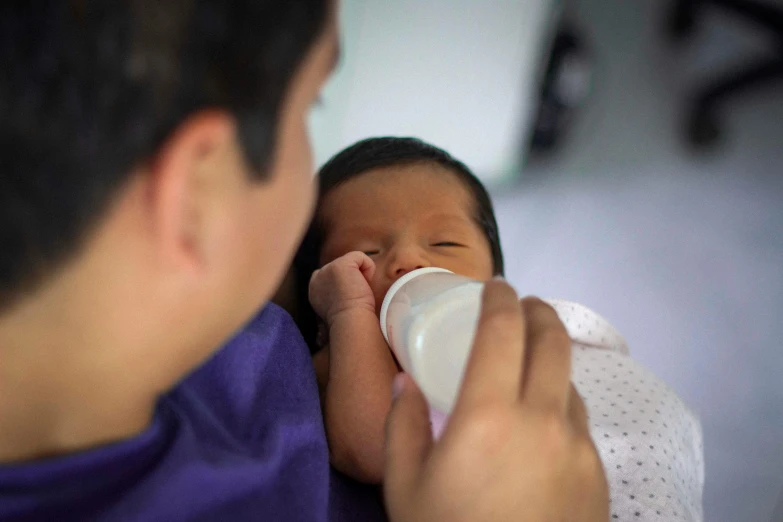 a woman holding a newborn baby drinking from a bottle