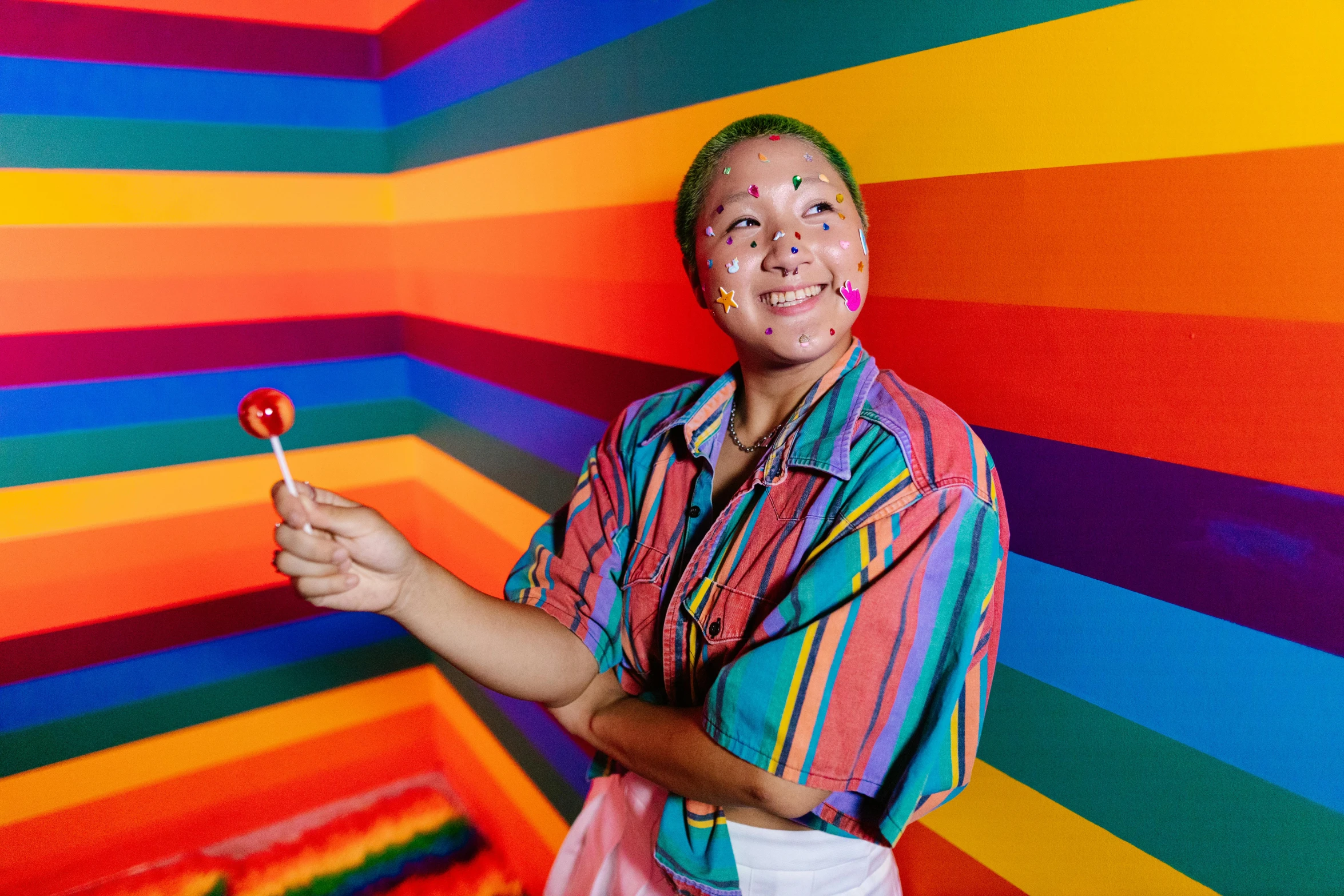 the man is wearing a rainbow outfit and holding up a lollipop