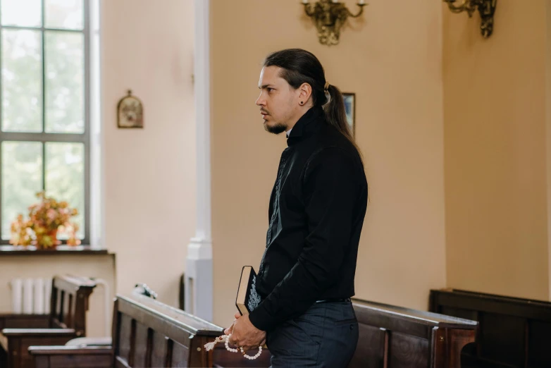man with long black hair standing at a church