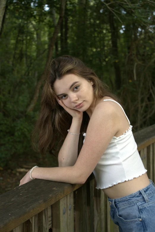 girl in jeans leaning on a fence with her hand on her chin