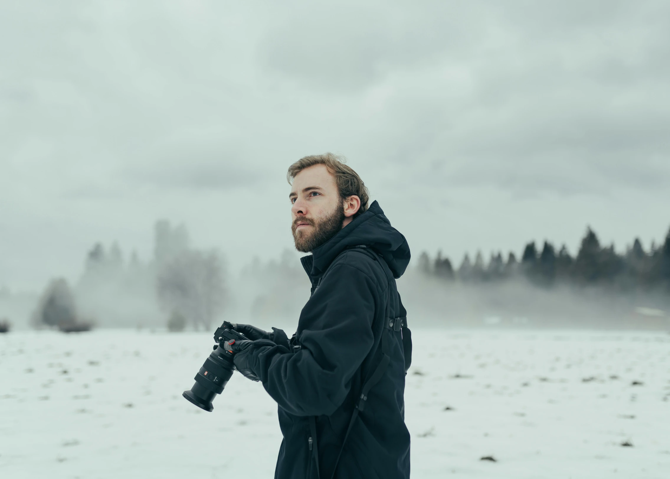 man in black coat and a black camera taking pictures of snow