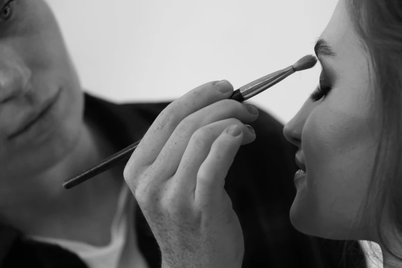 black and white pograph of a man brushing a woman's long nose with a brush