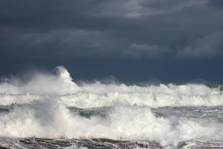 large waves crashing on to shore on a cloudy day