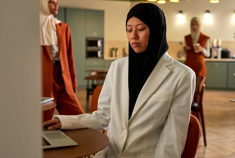 a young woman in white blazer sitting at a wooden table