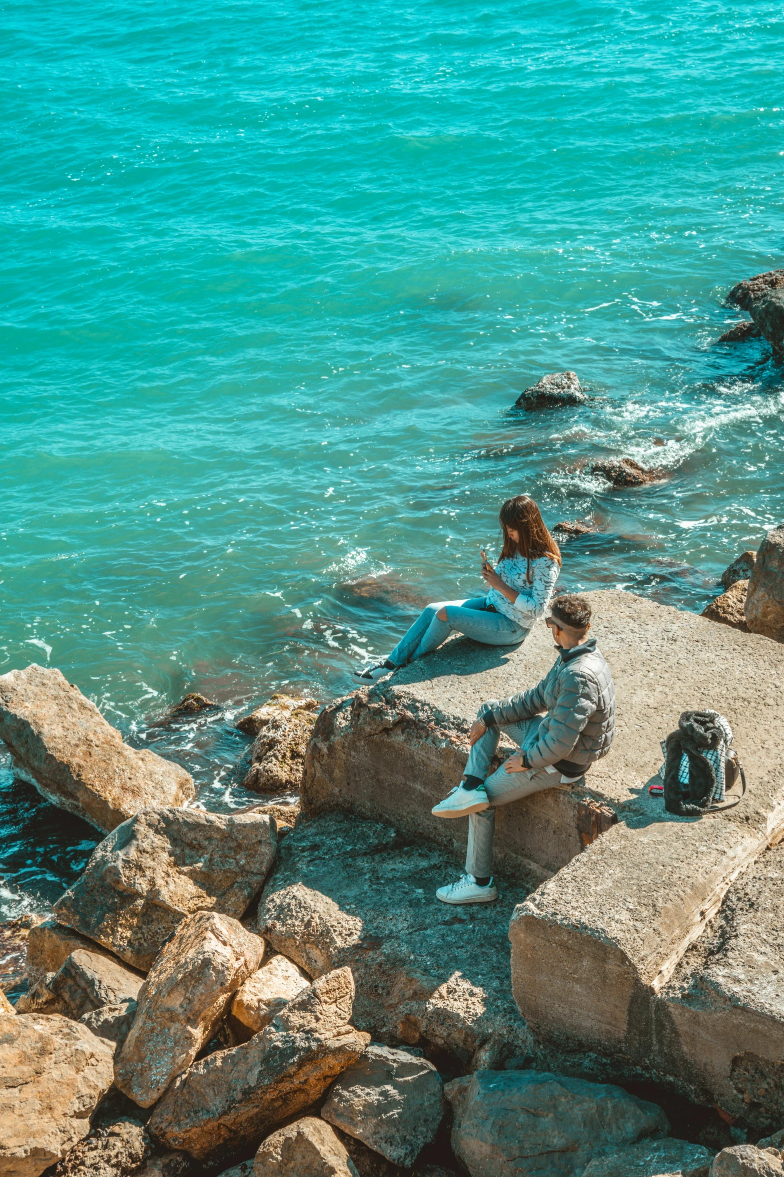 a man and woman sit on the rocks by the water