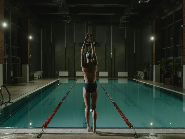 a person in a swim suit stands on their legs next to the edge of a swimming pool and lifts a ball to the air