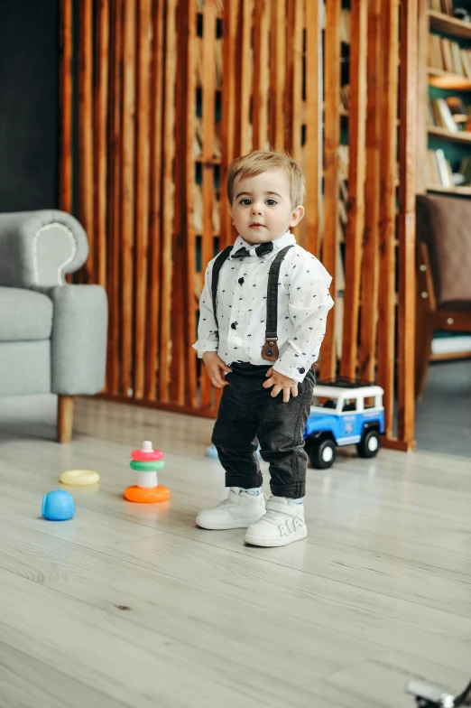 a young toddler with a tie and a bow tie standing in front of plastic toy cars