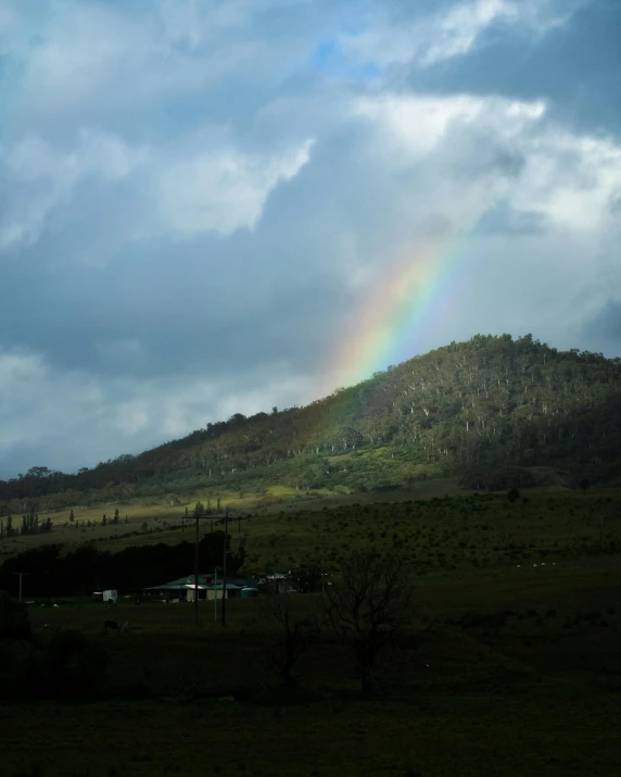 a beautiful rainbow arches over a hill on a gloomy day